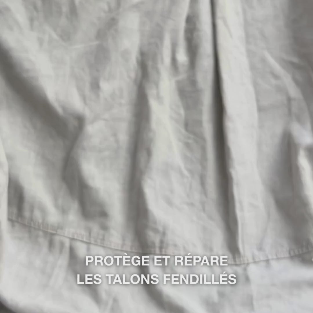 Gros plan sur une main prélevant une texture riche et crémeuse du Heel Repair et la massant doucement sur la peau sèche et fissurée du talon : la consistance épaisse est visiblement absorbée, adoucit et hydrate les zones rugueuses, tandis que l’urée à 25 %, le beurre de karité et l’huile d’arbre à thé apaisent et protègent la peau.