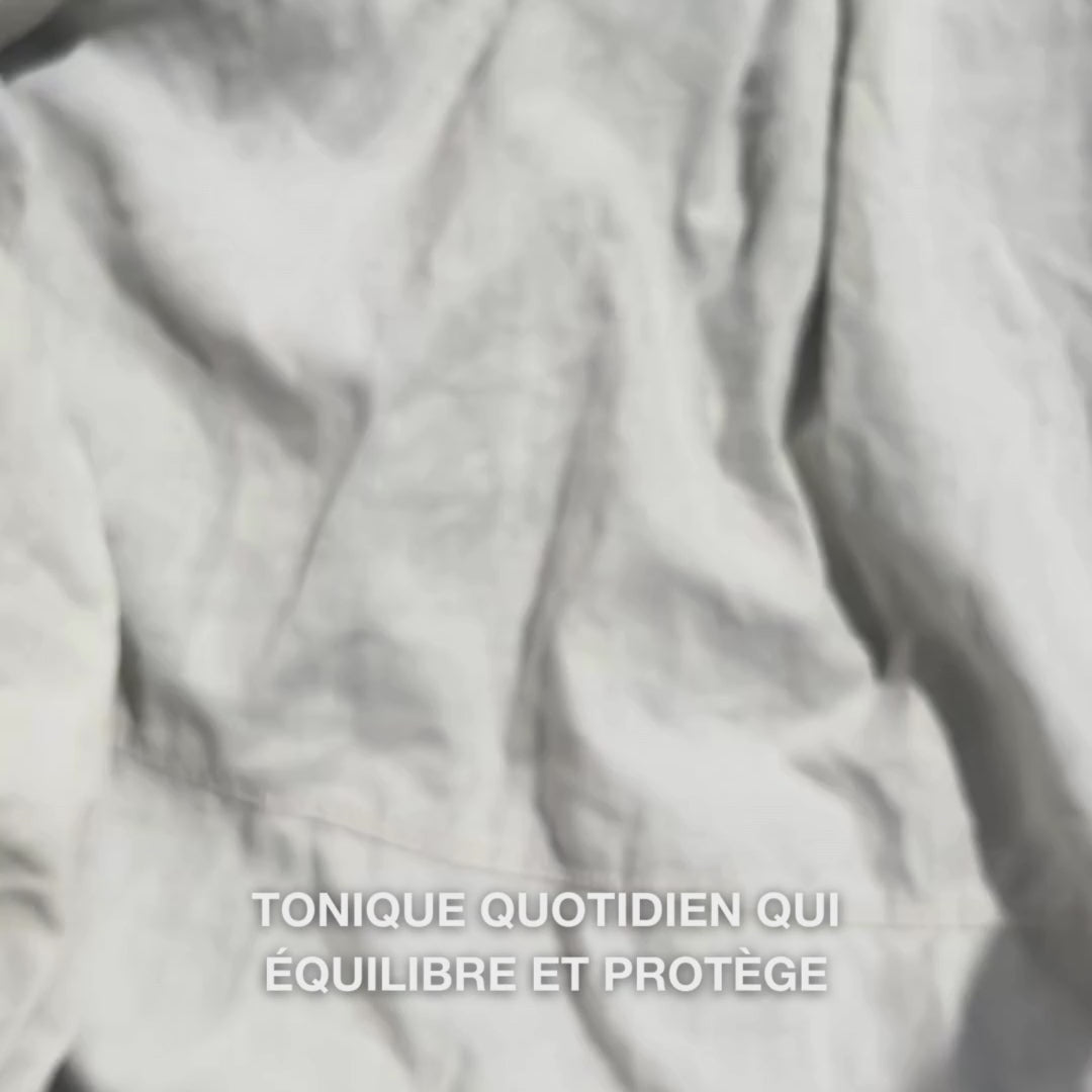 Gros plan d'une main déposant quelques gouttes du tonique transparent et aqueux enrichi à l’huile d’arbre à thé sur un coton, puis l’appliquant délicatement sur une peau nettoyée : le fluide léger et rafraîchissant apaise, nettoie en profondeur, hydrate et laisse la peau revitalisée et prête pour la crème.