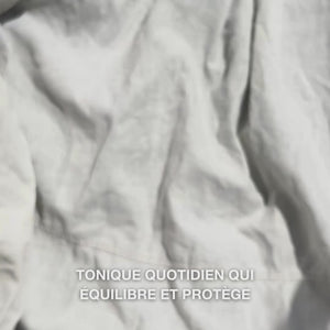 Gros plan d'une main déposant quelques gouttes du tonique transparent et aqueux enrichi à l’huile d’arbre à thé sur un coton, puis l’appliquant délicatement sur une peau nettoyée : le fluide léger et rafraîchissant apaise, nettoie en profondeur, hydrate et laisse la peau revitalisée et prête pour la crème.